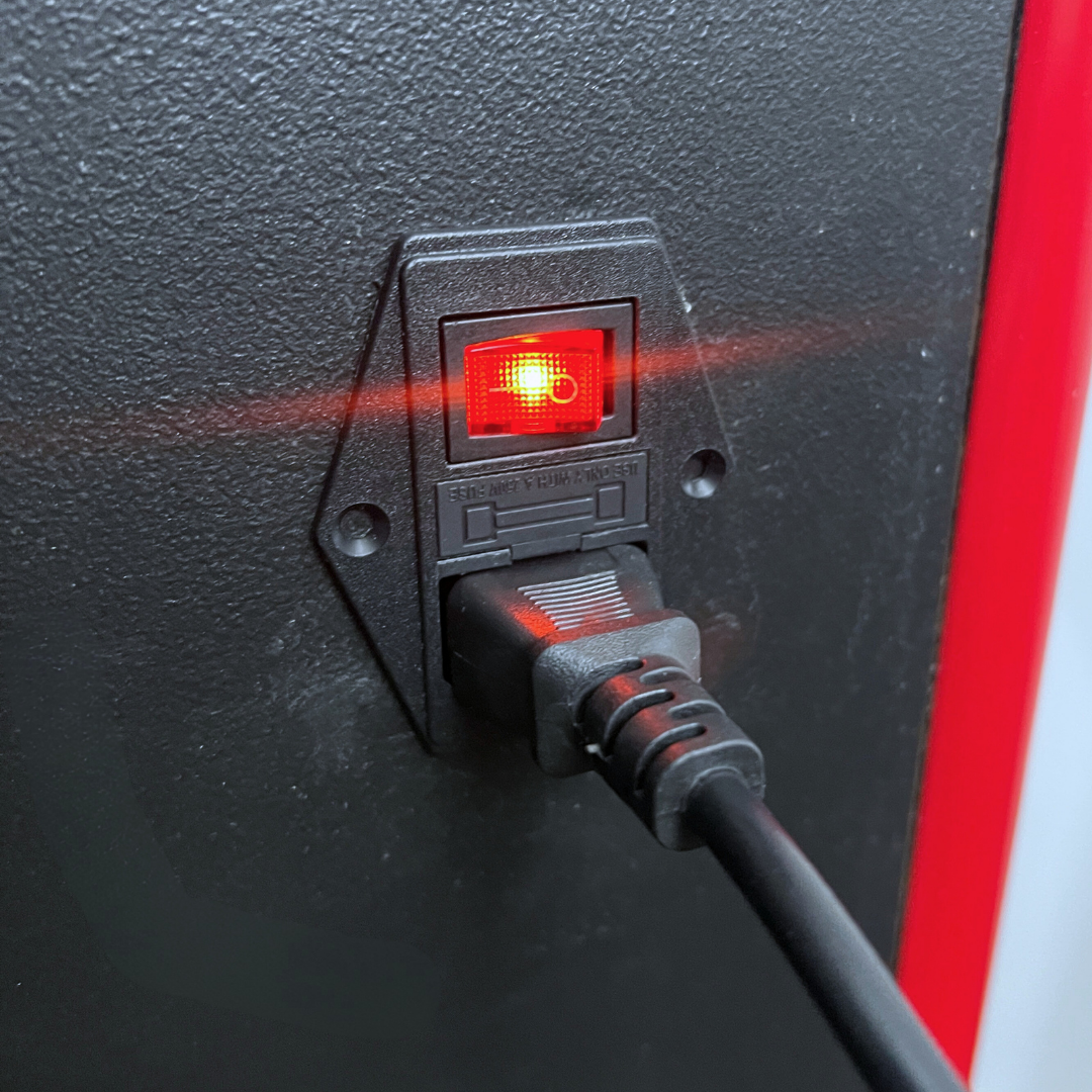 C14 Power outlet with compatible IEC cable plugged in with red light indicator on a back of arcade machine by Arcade Revival