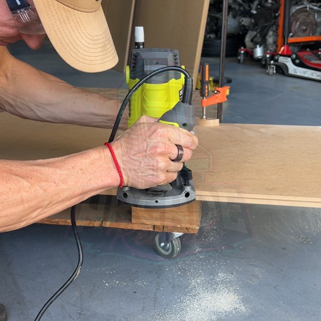 Person using a router to cut MDF arcade cabinet side panel during arcade machine build, part of the Arcade Revival DIY guide.