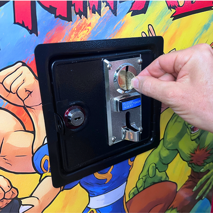 Single arcade coin acceptor installed in a black coin door on a finished arcade revival cabinet, with a coin being inserted.