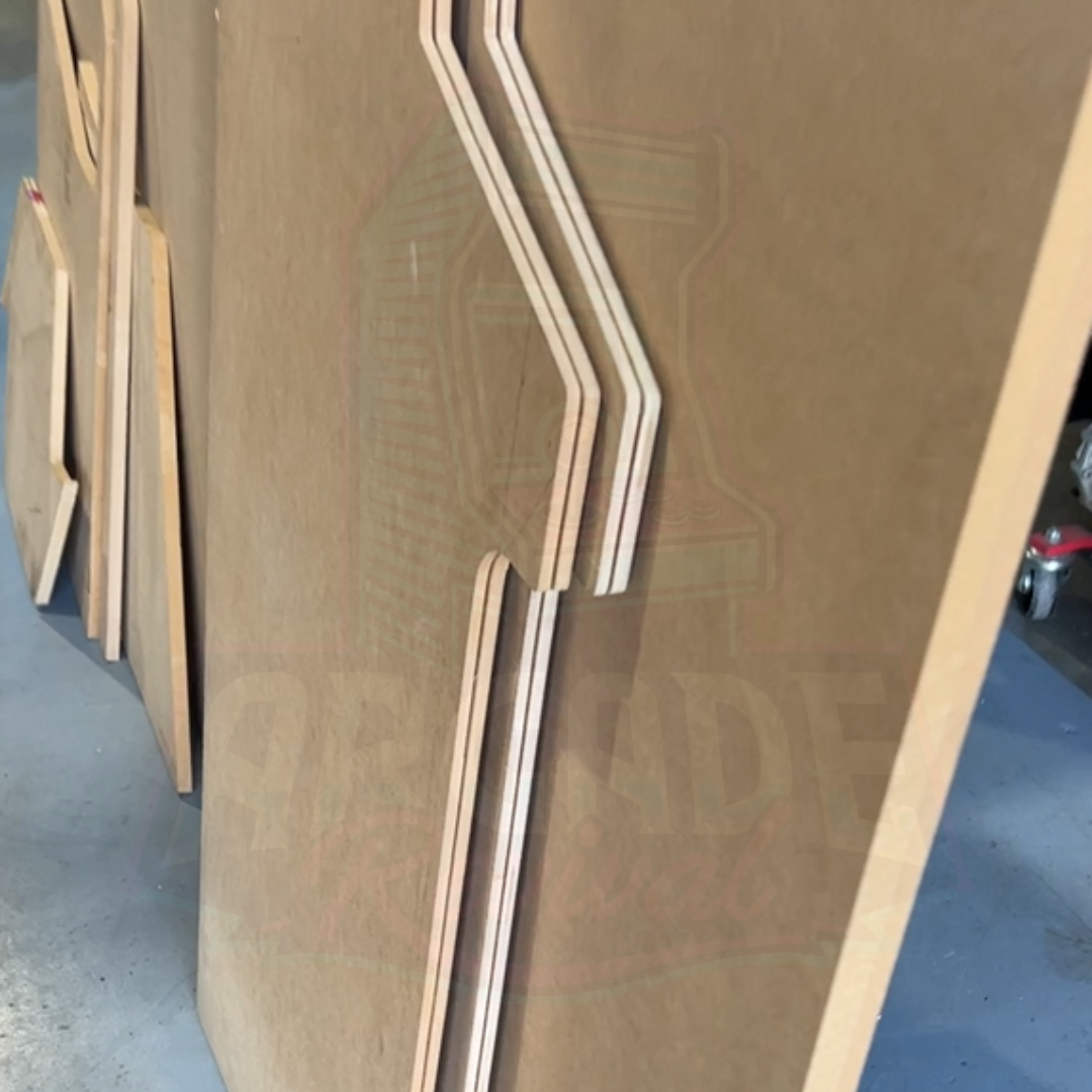 Pre-cut MDF arcade machine side panels stacked together showing routed T-moulding slots along edges