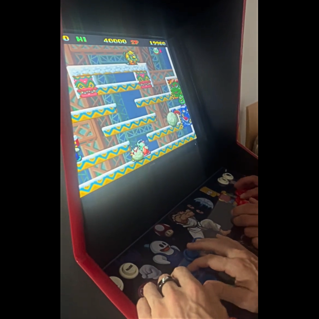 Close-up of two players enjoying a session of Snow Bros on a custom Arcade Revival machine, showing the themed control panel and arcade screen in action.
