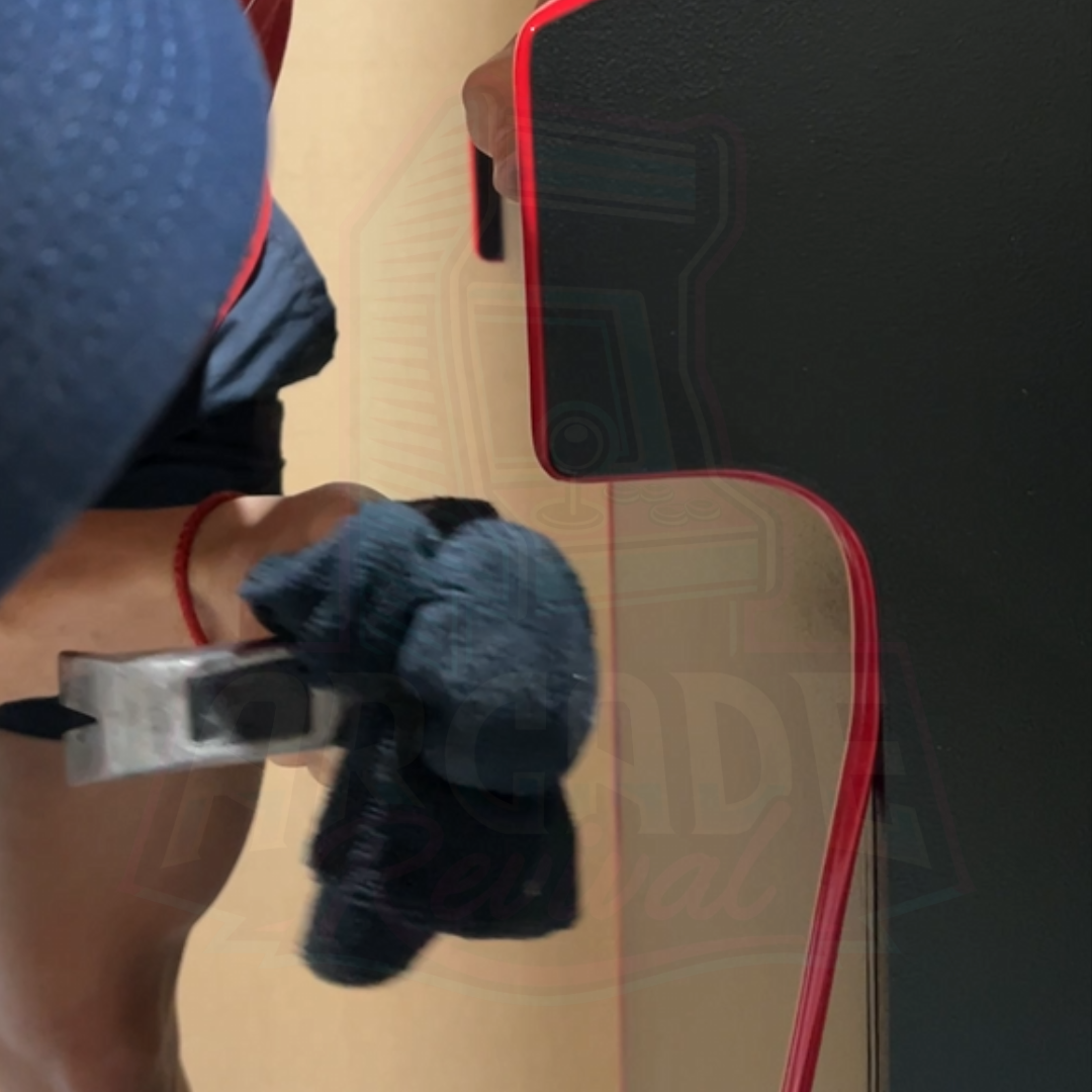 Fitting red T-moulding into an arcade cabinet side panel using a cloth and tool for a snug fit